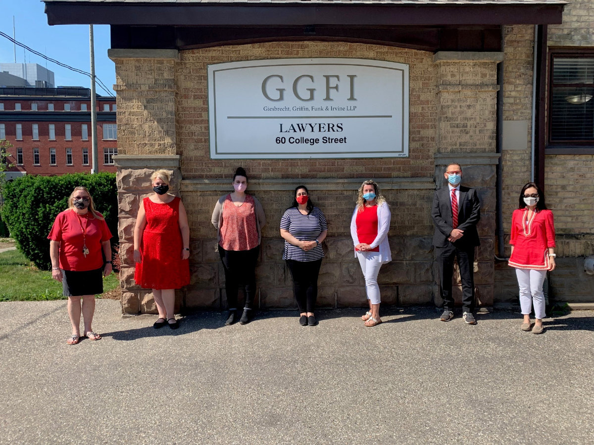 GGFI team dressed in red standing in front of a brick wall with the logo.